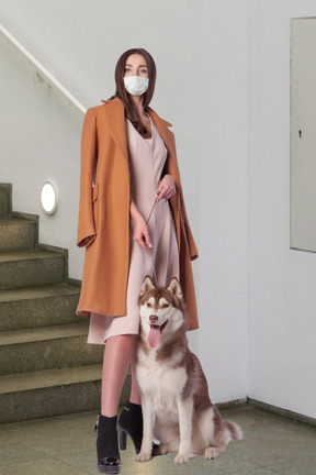 A woman wearing a face mask standing next to a dog