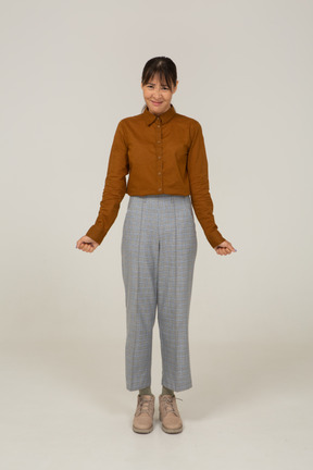 Vista frontal de una joven mujer asiática decepcionada en calzones y blusa apretando los puños