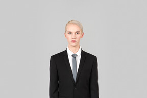 黒のフォーマルなスーツとネクタイを着た見栄えの良い若い男は、単に無地の灰色の背景に立っています