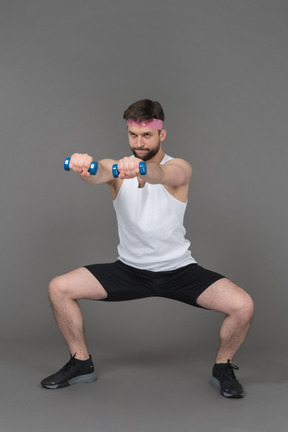 Hombre haciendo sentadilla con los brazos extendidos y sosteniendo pesas