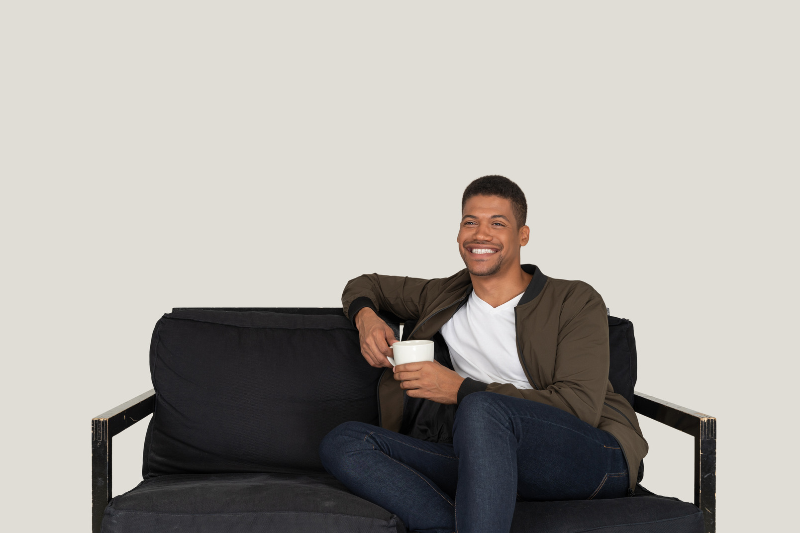 Front view of a smiling young man sitting on a sofa with a cup of coffee