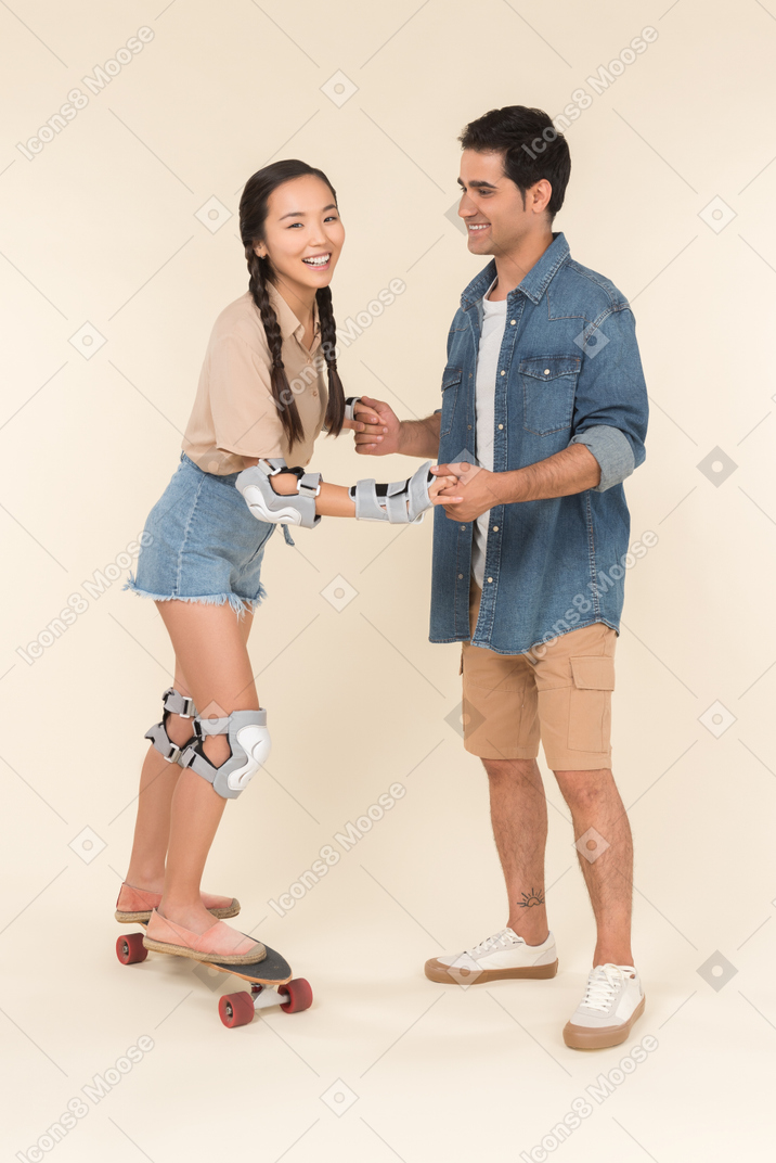 Young caucasian guy teaching asian girl how to skate