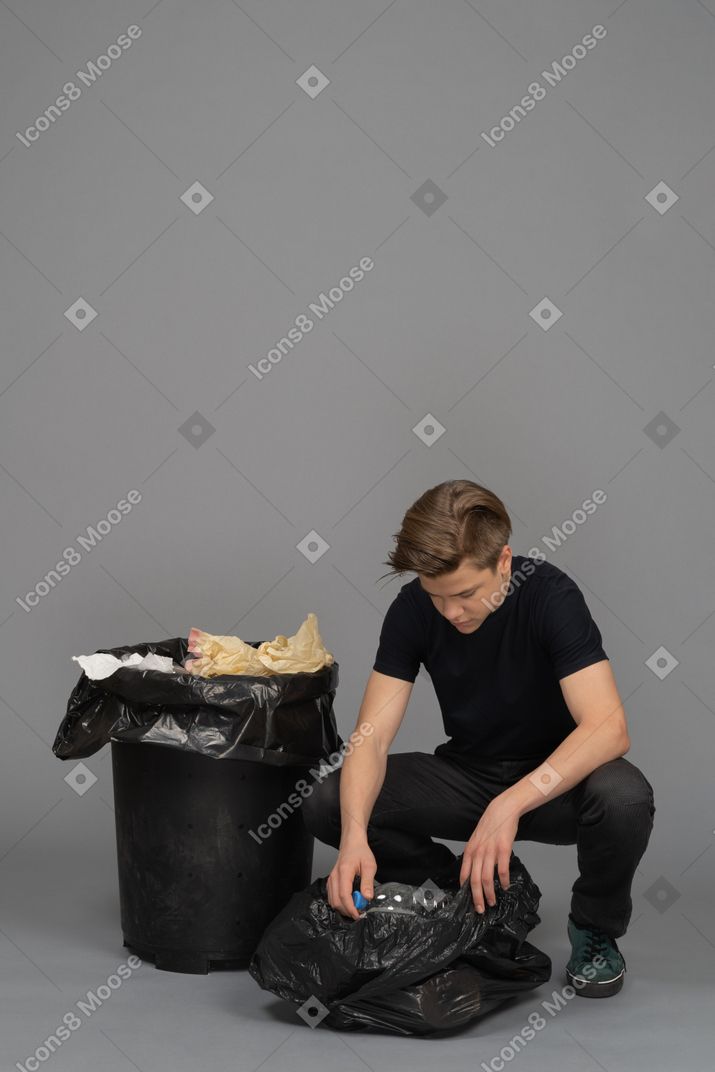 Un giovane uomo che carica una bottiglia di plastica in un sacco della spazzatura