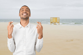 A man standing on a beach with his fingers crossed