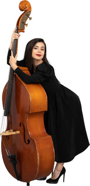 一位年轻的女音乐家，穿着黑色连衣裙，抱着她的双低音向前倾的四分之三的视图