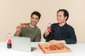 Amigos interraciales comiendo comida chatarra y viendo películas en la computadora portátil