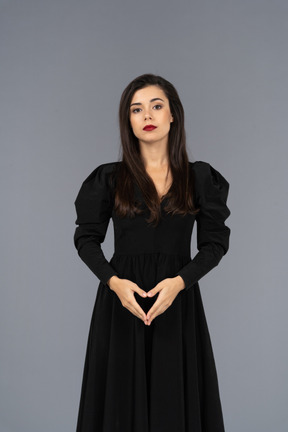 Vista frontale di una giovane donna prepotente in un vestito nero che tengono le mani insieme