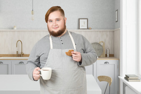 A bearded man in an apron holding a cup of coffee