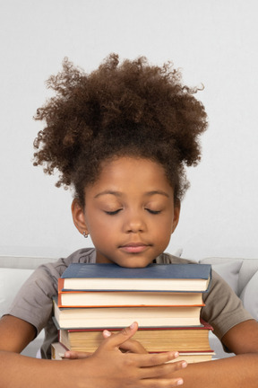 Niña sosteniendo un montón de libros con los ojos cerrados