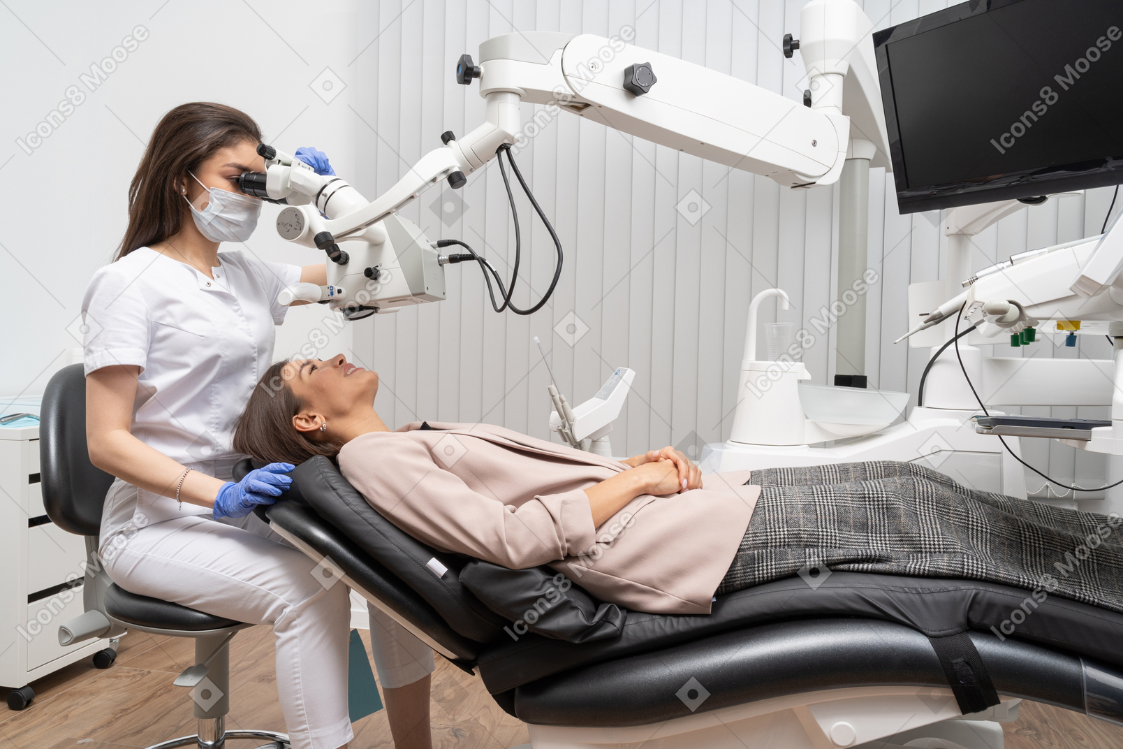 Женщина-стоматолог в полный рост осматривает свою пациентку и смотрит в микроскоп