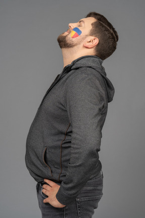 Side view of a tired male football fan with colorful face art leaning back