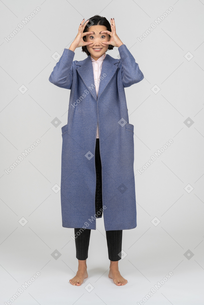 Young asian woman in long blue coat opening her eyes with hands