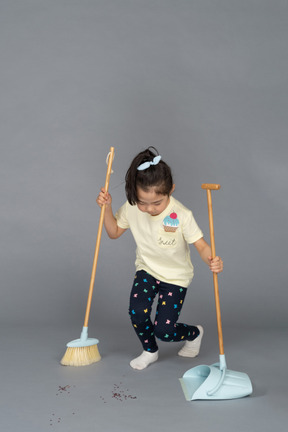 Portrait en pied d'une petite fille penchée en avant pour balayer le sol