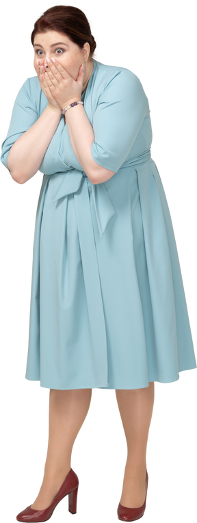 Front view of a shocked woman in blue dress covering mouth with hands