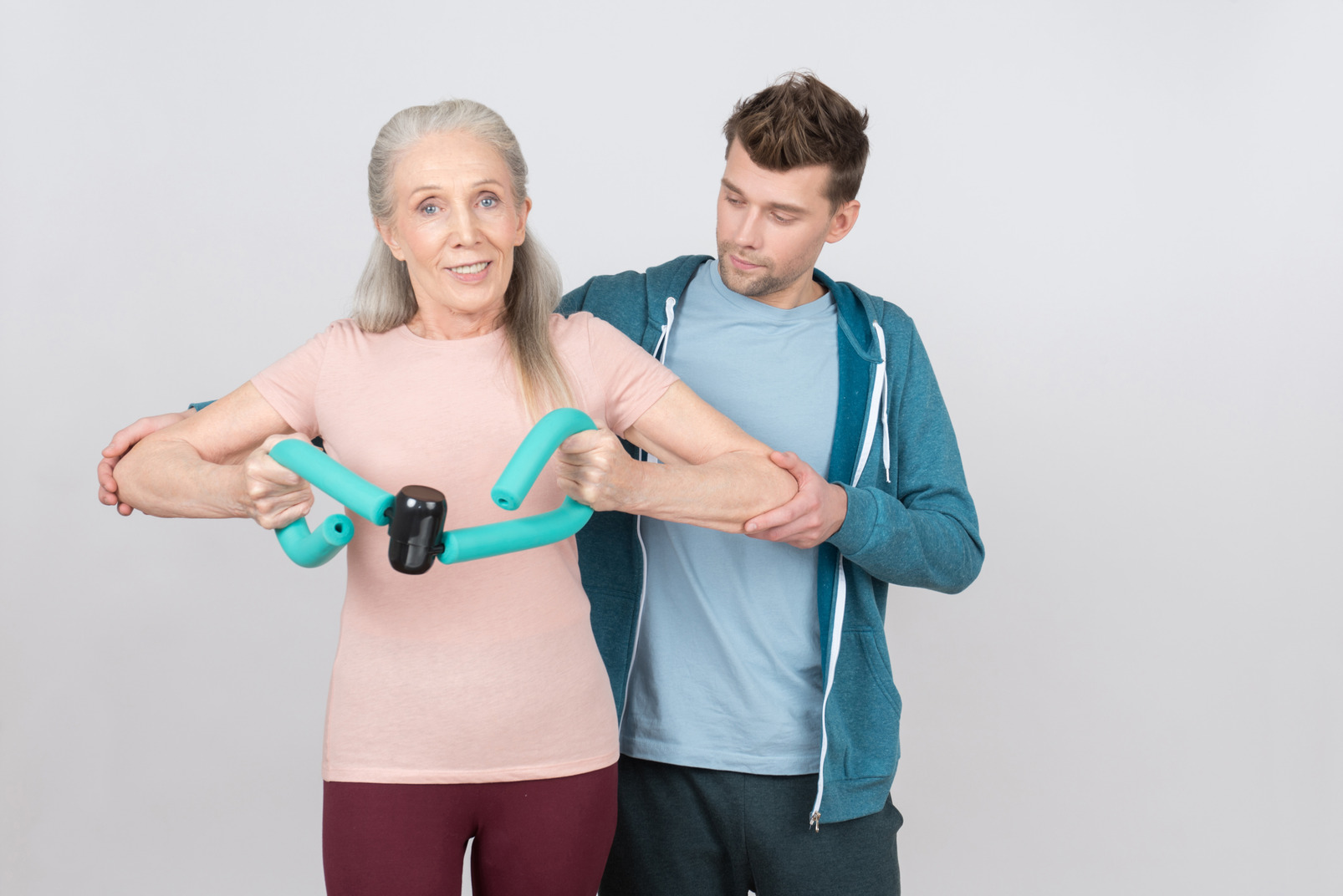 Young gym teacher helps old woman to deal with expander exercise