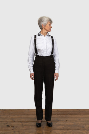 Vista frontal de uma mulher idosa com roupas de escritório, parada dentro de casa, olhando para o lado