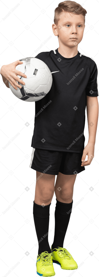 Vista de três quartos de uma criança menino em uniforme de futebol segurando uma bola e olhando para o lado