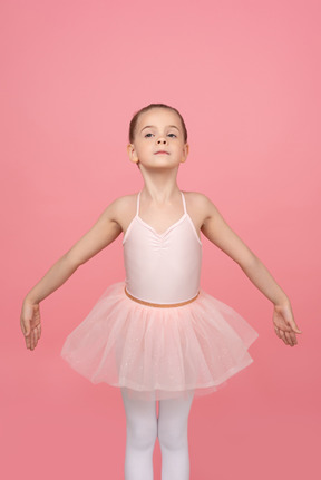 Little dancer with serious face standing with her hands wide aside