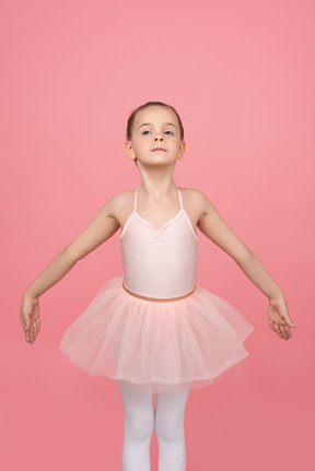 Pequeña bailarina con rostro serio de pie con las manos a un lado.