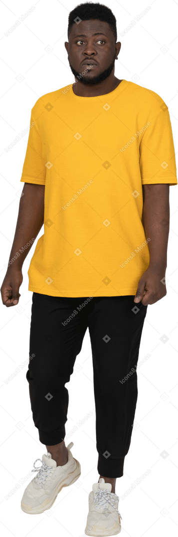 Front view of a puzzled young dark-skinned man in yellow t-shirt looking aside