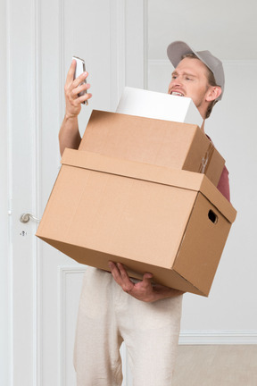 A man holding a cardboard box and a cell phone