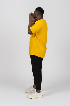 Vista laterale di un giovane uomo dalla pelle scura urlante in maglietta gialla