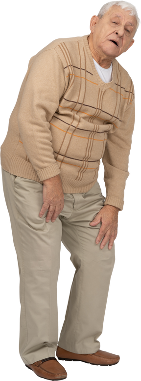 Vista frontal de un anciano con ropa informal tocando su rodilla lastimada