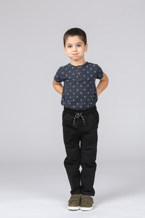 Vista frontal de un chico lindo en ropa casual posando con las manos detrás de la espalda