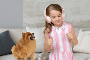A little girl listening to headphones while standing next to a dog