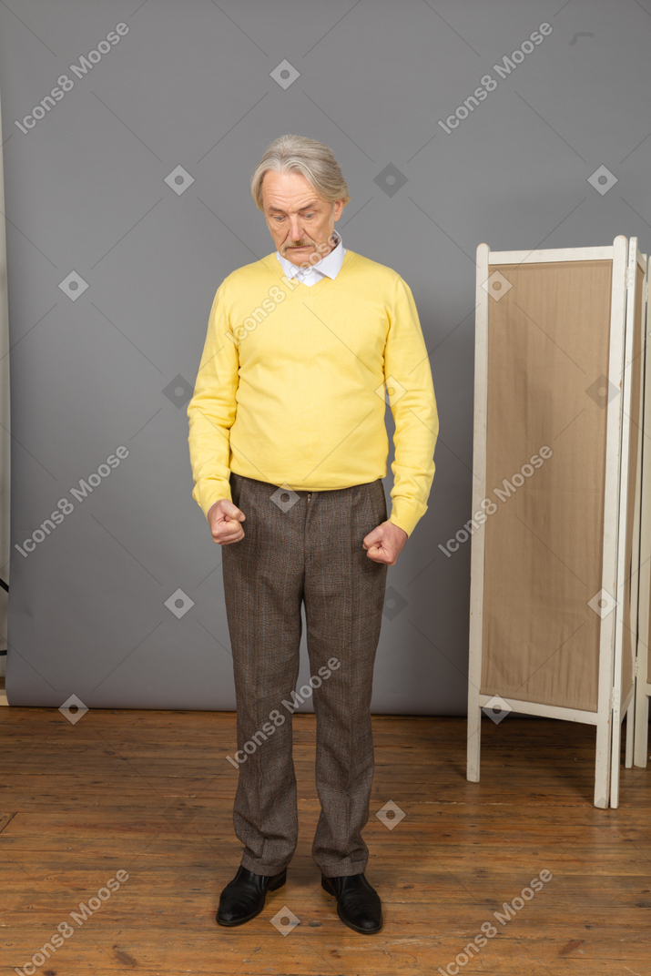 Front view of a strong old man clenching fists while looking down