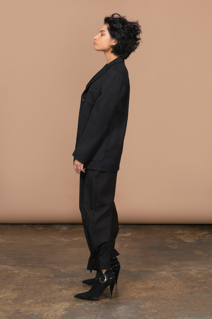 Side view of a sleepy businesswoman in a black suit standing with her eyes closed