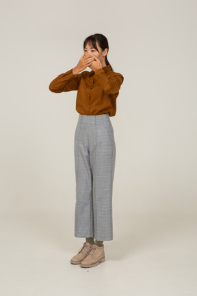 Three-quarter view of a young asian female in breeches and blouse hiding mouth