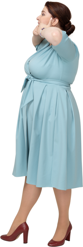 Vista lateral de uma mulher de vestido azul tocando a boca