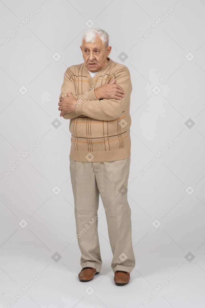 Front view of an old man in casual clothes hugging himself