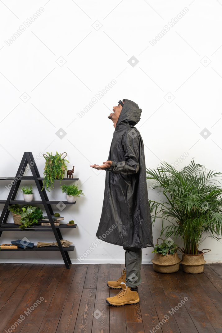 Vue latérale d'un homme en imperméable attrapant des gouttes de pluie