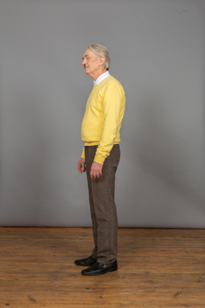 Vista de três quartos de um homem velho de pulôver amarelo olhando para o lado