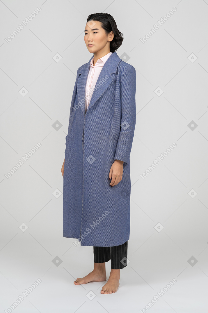 긴 파란색 코트 절반 옆으로 서있는 젊은 아시아 여자