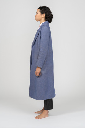 Side view of a woman in coat with puffed out cheeks