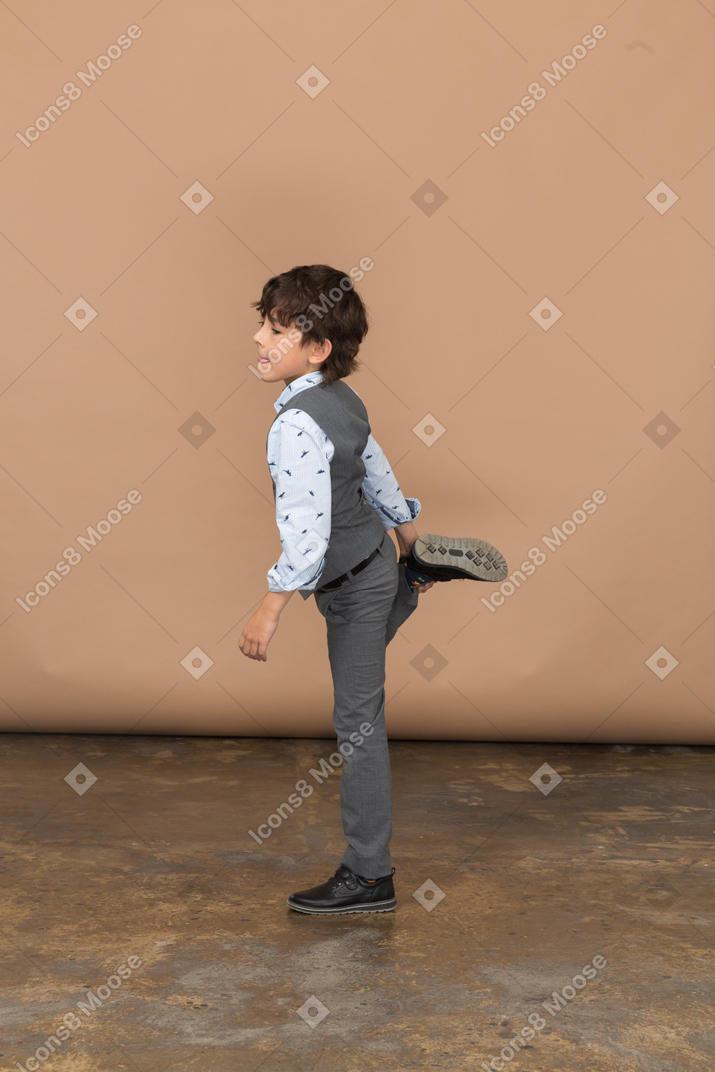 Vista laterale di un ragazzo in abito grigio in posa su una gamba