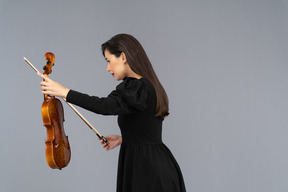 Vista lateral de una violinista femenina en vestido negro haciendo una reverencia