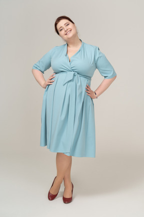 Vista frontal de una mujer feliz en vestido azul posando con las manos en las caderas