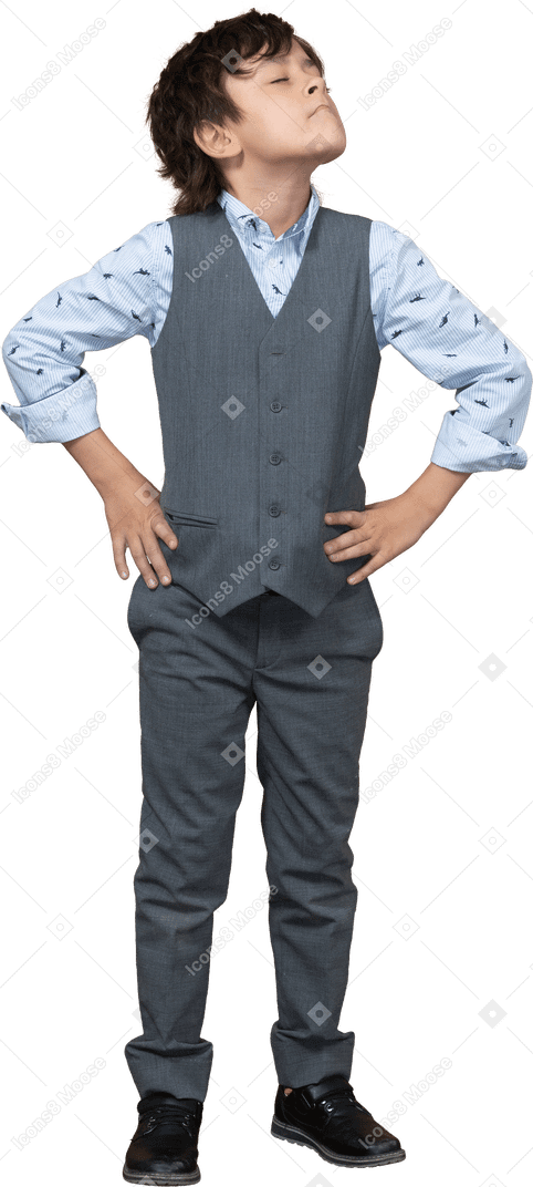 Vista frontal de un chico lindo con traje gris posando con las manos en las caderas y mirando hacia arriba