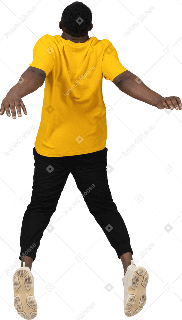 Vista traseira de um jovem de pele escura pulando em uma camiseta amarela estendendo as mãos