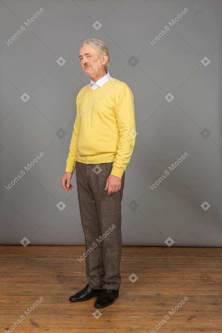 Vista de três quartos de um velho triste com um casaco amarelo olhando para a câmera