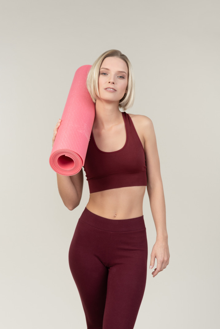 Young woman holding yoga mat on her shoulder