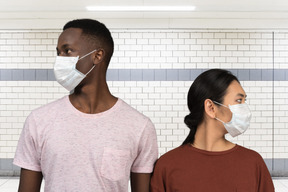 Junges interracial paar, das medizinische masken trägt und beiseite schaut