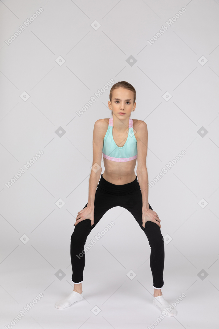 一个十几岁的女孩在运动服蹲着，把手放在臀部上的侧视图