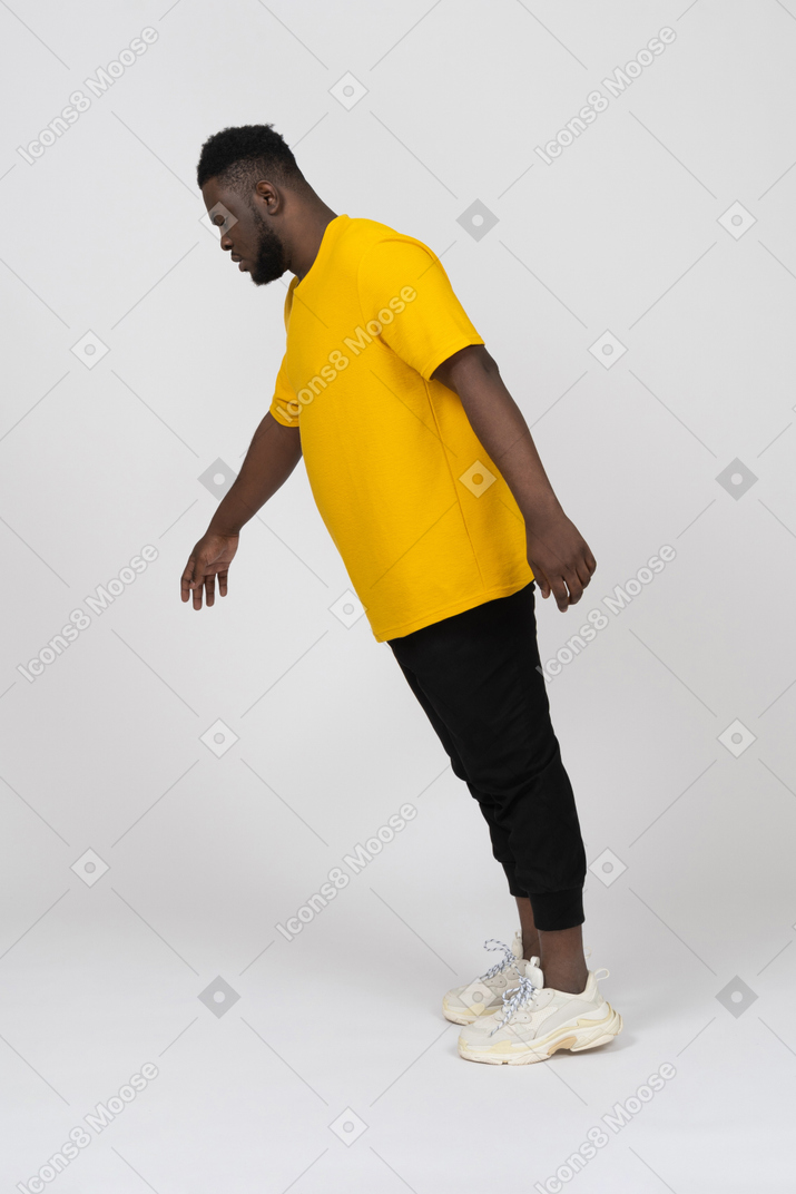 Side view of a young dark-skinned man in yellow t-shirt leaning forward & outstretching arm