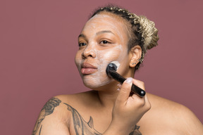 Beautiful plump afro woman applying a face cream with brush