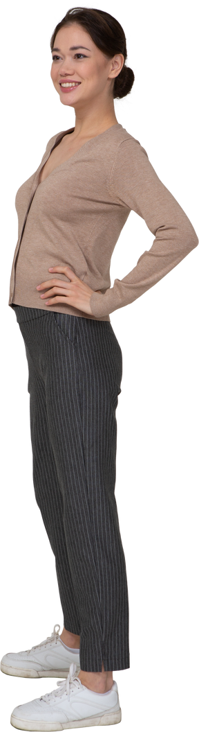 Vue de trois quarts d'une jeune femme souriante en pull et pantalon mettant les mains sur les hanches